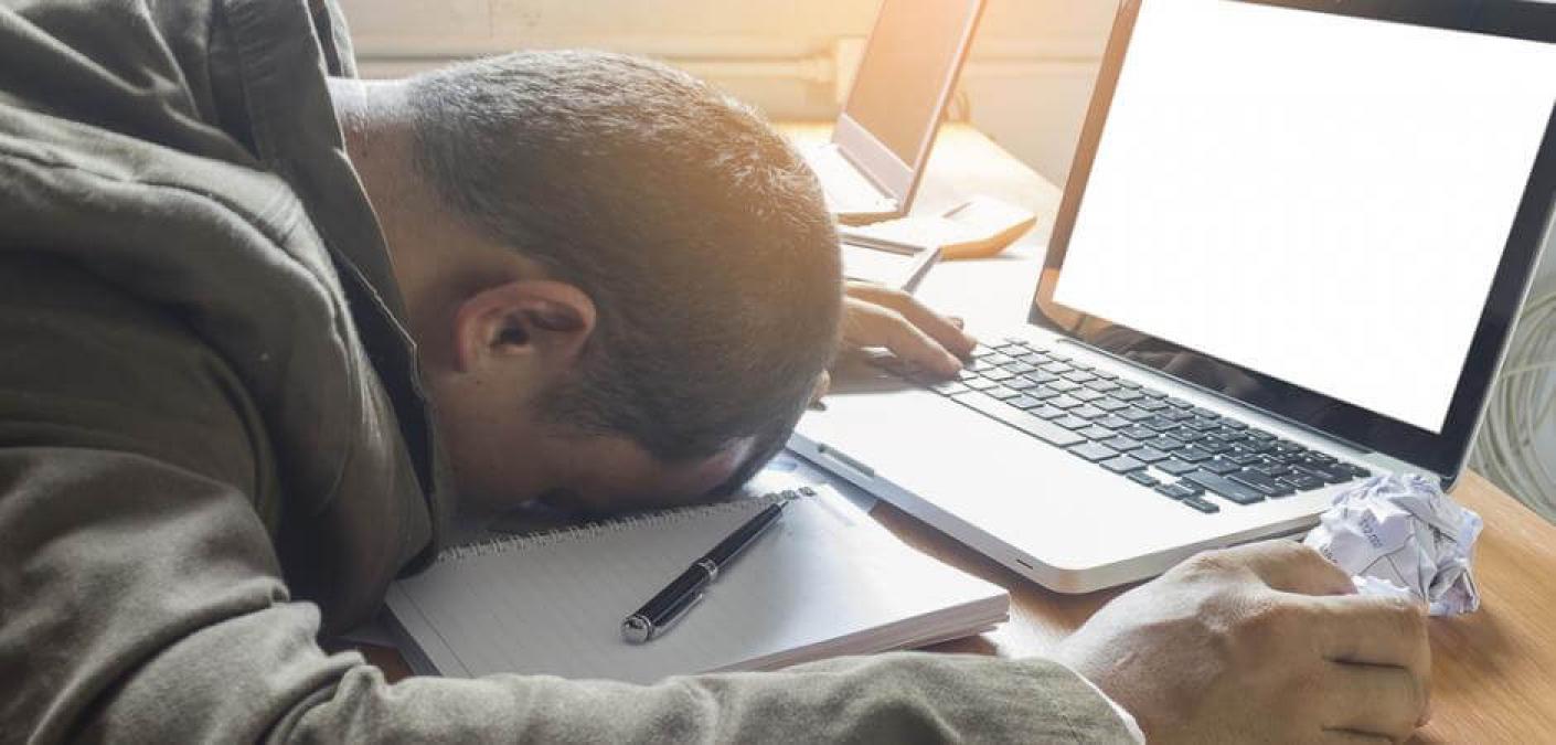 man with head on desk next to laptop