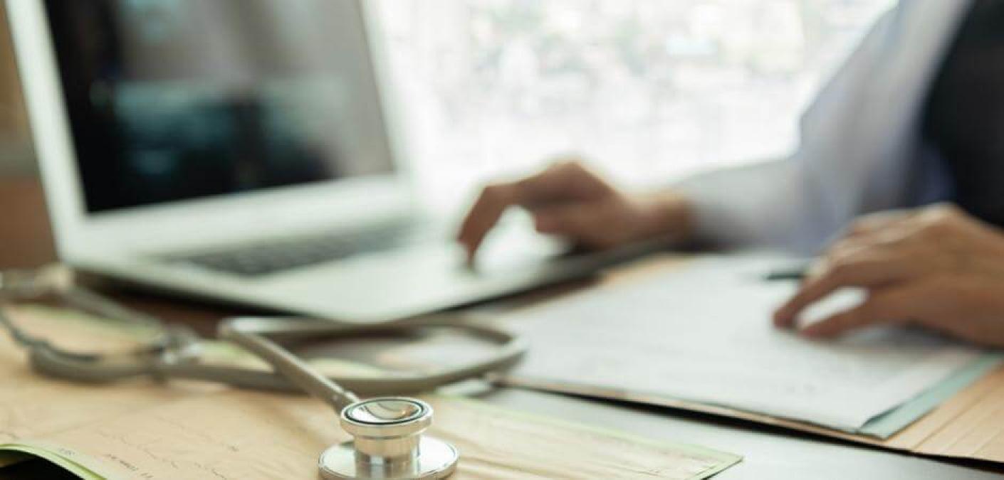 person using laptop next to stethoscope